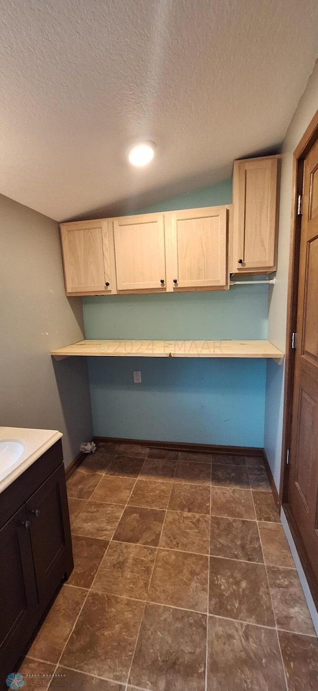 kitchen featuring light brown cabinets, a textured ceiling, dark tile patterned floors, and built in desk