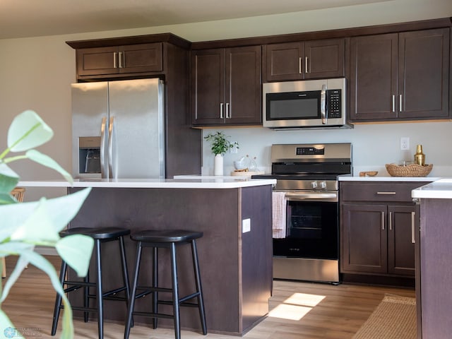 kitchen with dark brown cabinets, light hardwood / wood-style floors, a kitchen bar, and stainless steel appliances