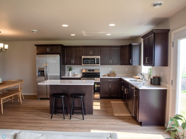 kitchen with a center island, a kitchen bar, light hardwood / wood-style flooring, an inviting chandelier, and appliances with stainless steel finishes