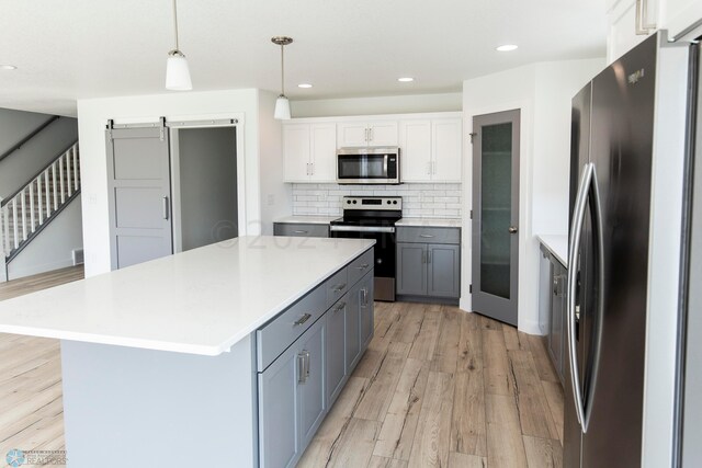 kitchen featuring decorative light fixtures, white cabinets, light hardwood / wood-style flooring, backsplash, and appliances with stainless steel finishes