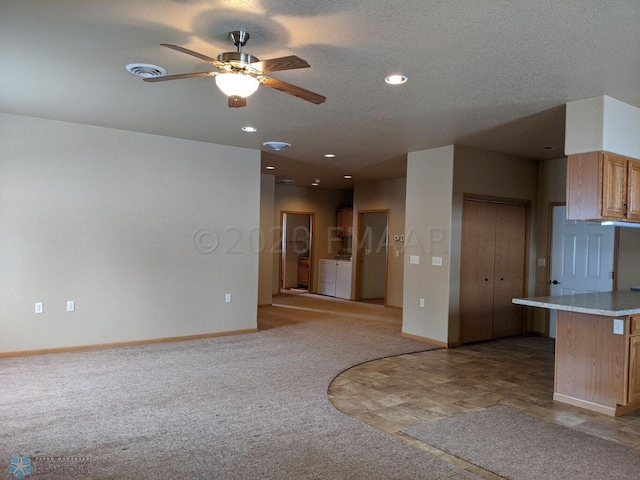 unfurnished living room featuring washing machine and dryer, ceiling fan, light tile floors, and a textured ceiling