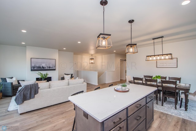 kitchen with a kitchen island, light hardwood / wood-style flooring, light stone counters, and decorative light fixtures