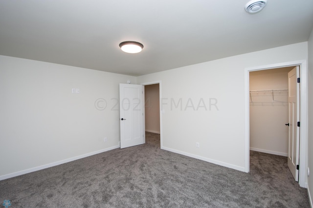 unfurnished bedroom featuring a closet, a spacious closet, and dark carpet