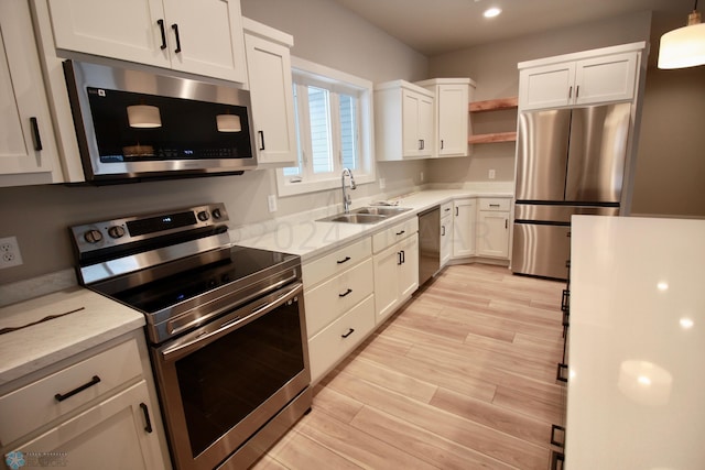 kitchen with appliances with stainless steel finishes, light hardwood / wood-style floors, light stone counters, white cabinets, and sink