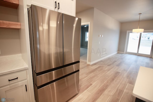 kitchen with pendant lighting, white cabinets, stainless steel fridge, and light wood-type flooring