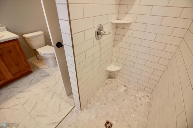 bathroom with tiled shower, tile flooring, vanity, and toilet