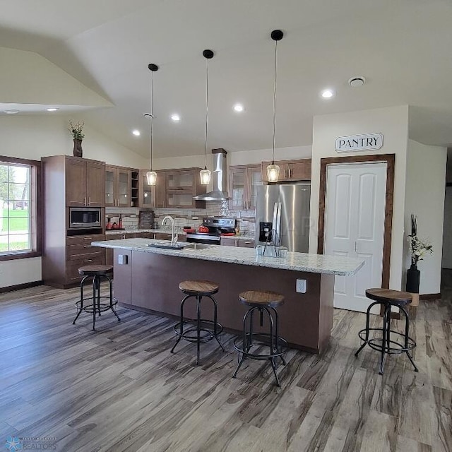 kitchen with appliances with stainless steel finishes, wood-type flooring, wall chimney range hood, and a kitchen bar