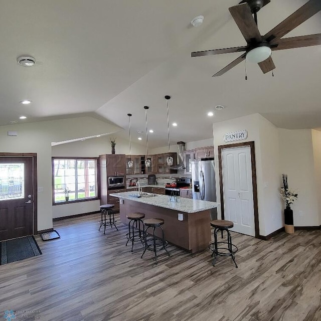 kitchen featuring a kitchen breakfast bar, wood-type flooring, a kitchen island with sink, vaulted ceiling, and ceiling fan