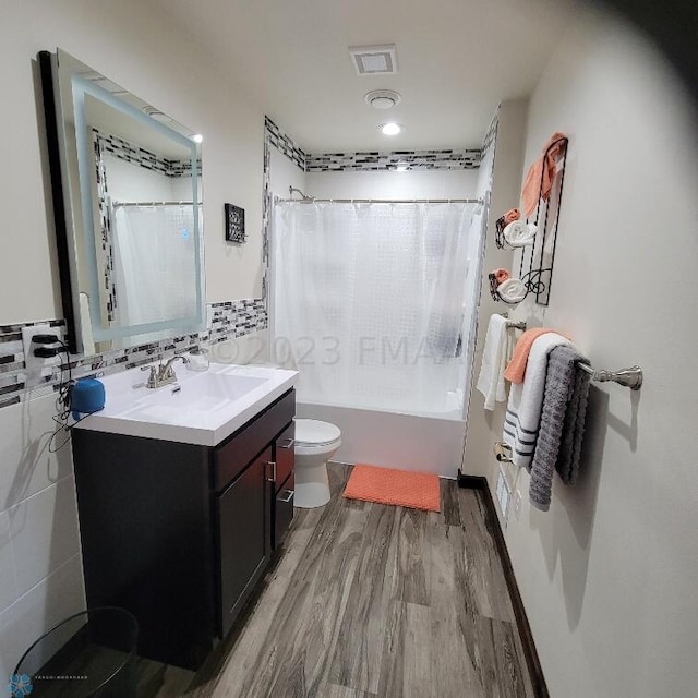 full bathroom with tile walls, large vanity, shower / bath combo, toilet, and hardwood / wood-style flooring