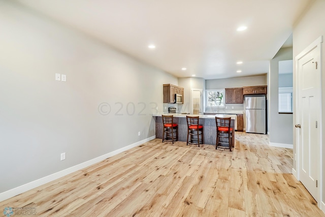 kitchen with a breakfast bar area, stainless steel appliances, kitchen peninsula, and light wood-type flooring