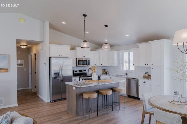 kitchen featuring appliances with stainless steel finishes, tasteful backsplash, white cabinetry, a center island, and light wood-type flooring