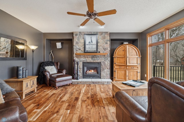 living room featuring a textured ceiling, a fireplace, wood-type flooring, and ceiling fan