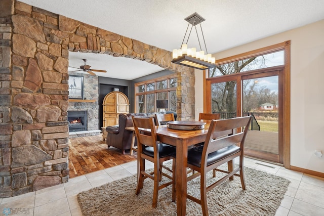 dining space with a stone fireplace, a textured ceiling, ceiling fan, and light wood-type flooring