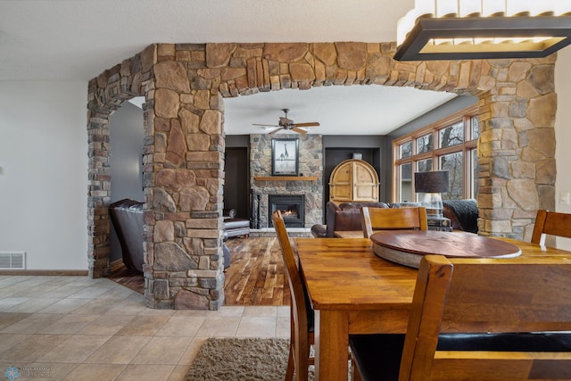 dining area with a stone fireplace, a textured ceiling, ceiling fan, and tile patterned floors