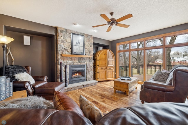 living room with a stone fireplace, light wood-type flooring, ceiling fan, and a textured ceiling