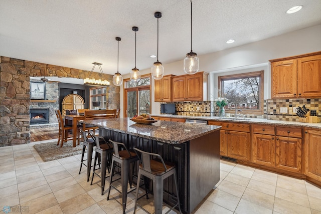 kitchen featuring decorative backsplash, a stone fireplace, a center island, and sink