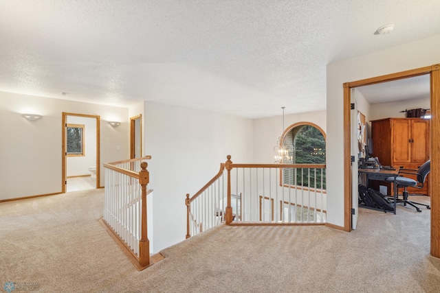 hall with light carpet, a chandelier, and a textured ceiling