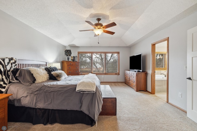 bedroom featuring a textured ceiling, connected bathroom, ceiling fan, light colored carpet, and a raised ceiling