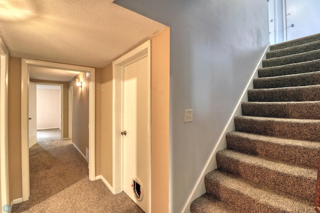 stairway with a textured ceiling and carpet