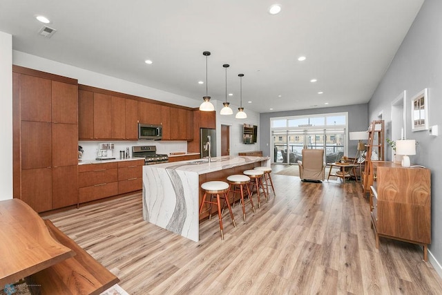 kitchen with a kitchen island with sink, a breakfast bar, decorative light fixtures, stainless steel appliances, and light hardwood / wood-style floors