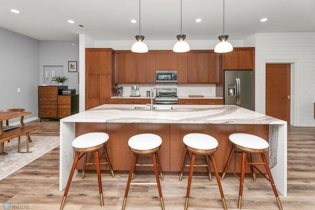 kitchen featuring stainless steel appliances, light hardwood / wood-style flooring, a center island with sink, and pendant lighting