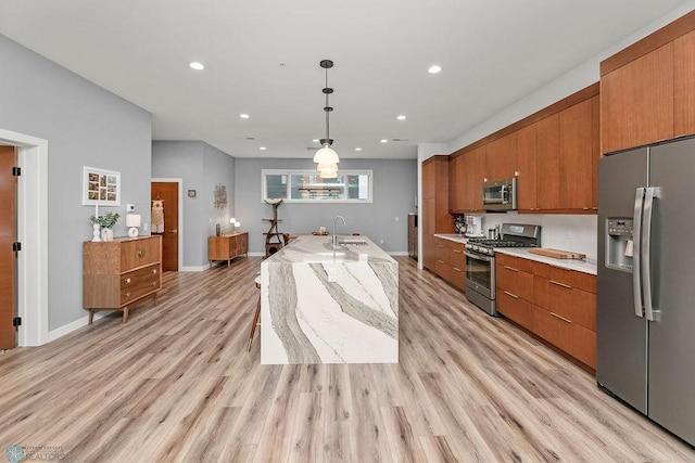 kitchen with hanging light fixtures, stainless steel appliances, light wood-type flooring, and a center island with sink