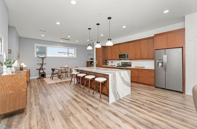 kitchen featuring appliances with stainless steel finishes, a kitchen island with sink, a kitchen bar, light hardwood / wood-style floors, and pendant lighting