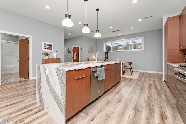 kitchen with light stone counters, appliances with stainless steel finishes, decorative light fixtures, light hardwood / wood-style flooring, and a kitchen island with sink