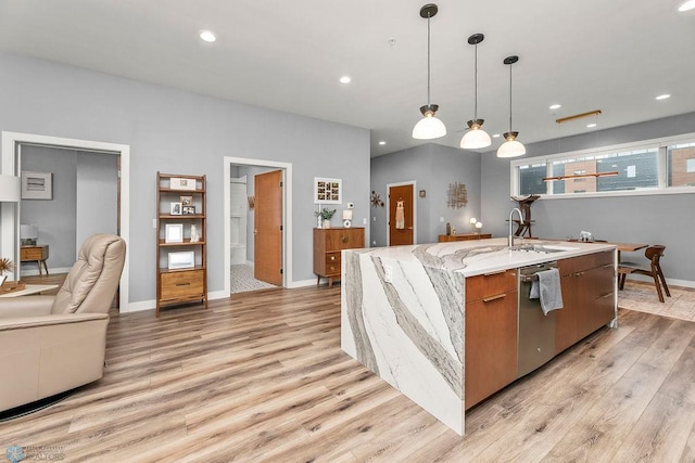 kitchen featuring decorative light fixtures, sink, light hardwood / wood-style flooring, and a kitchen island with sink