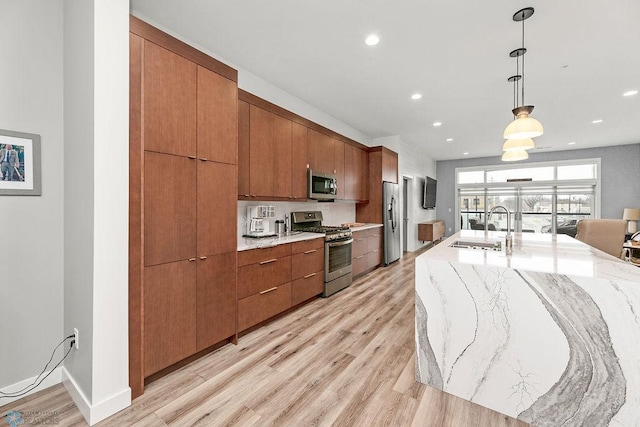 kitchen with hanging light fixtures, light stone countertops, light hardwood / wood-style flooring, stainless steel appliances, and sink