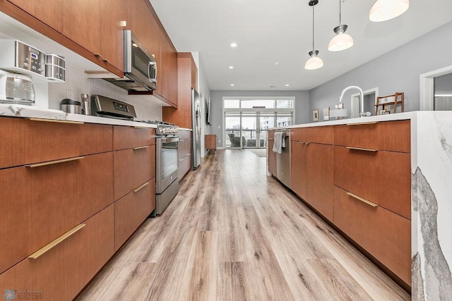 kitchen with pendant lighting, stainless steel appliances, and light wood-type flooring