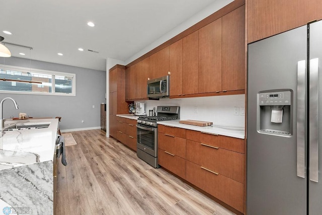 kitchen with light stone counters, appliances with stainless steel finishes, sink, and light wood-type flooring