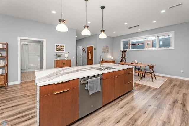 kitchen with decorative light fixtures, a center island with sink, dishwasher, sink, and light wood-type flooring