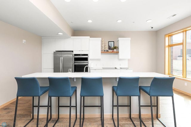 kitchen with appliances with stainless steel finishes, an island with sink, and white cabinetry