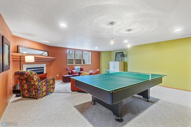 recreation room with carpet flooring, a textured ceiling, and a tiled fireplace