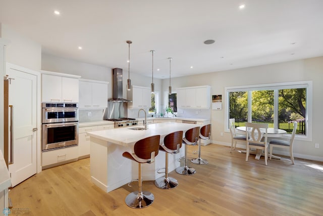 kitchen featuring decorative light fixtures, white cabinets, wall chimney exhaust hood, light hardwood / wood-style flooring, and backsplash