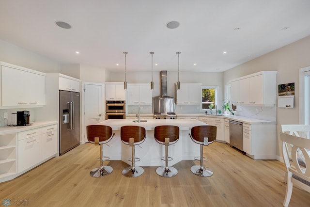 kitchen with white cabinetry, light wood-type flooring, wall chimney range hood, backsplash, and appliances with stainless steel finishes