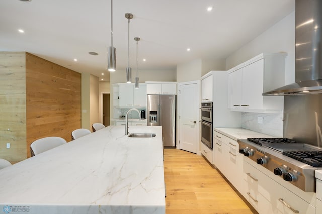 kitchen featuring appliances with stainless steel finishes, light hardwood / wood-style flooring, white cabinets, wall chimney range hood, and decorative backsplash