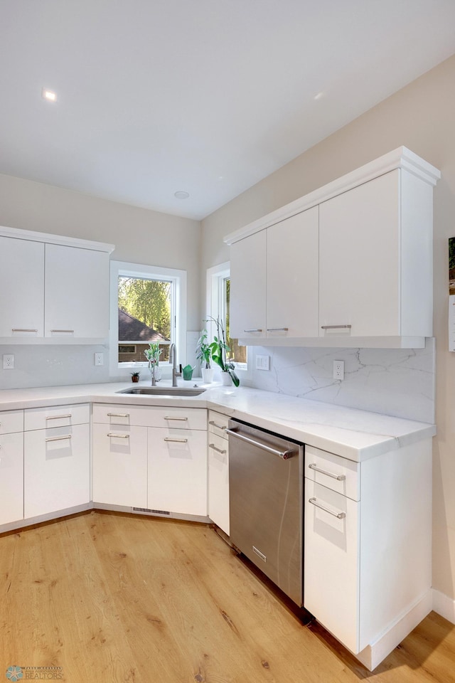 kitchen featuring white cabinetry, light wood-type flooring, backsplash, stainless steel dishwasher, and sink