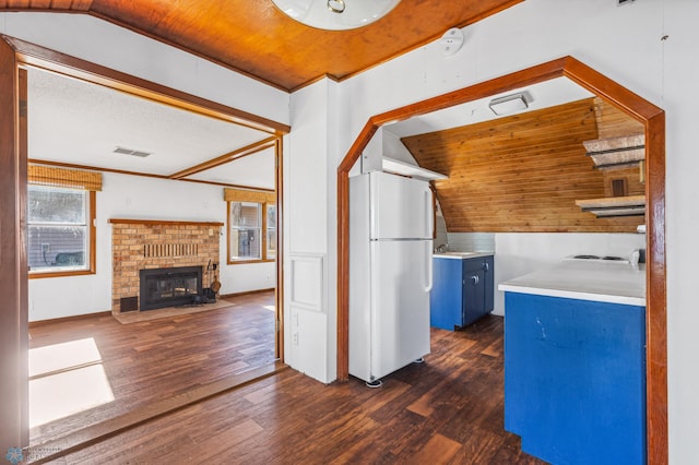 kitchen featuring a brick fireplace, dark hardwood / wood-style floors, white fridge, blue cabinetry, and vaulted ceiling