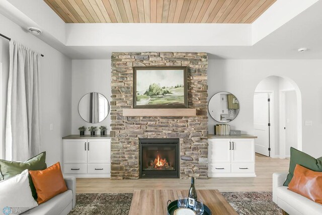 living room with wooden ceiling, light hardwood / wood-style floors, a stone fireplace, and a tray ceiling