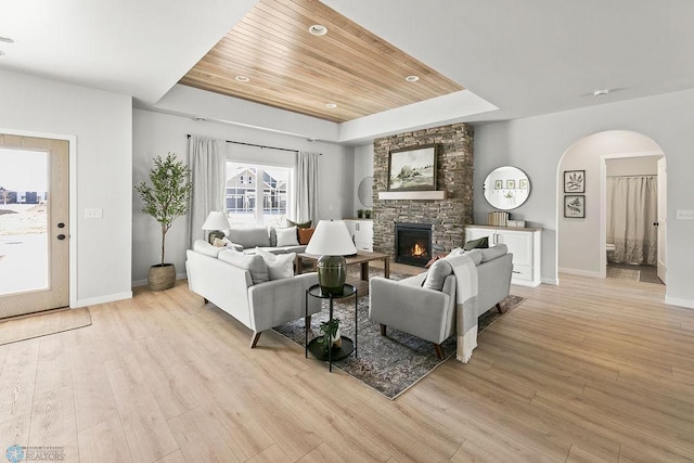 living room with wood ceiling, a tray ceiling, light hardwood / wood-style floors, and a stone fireplace