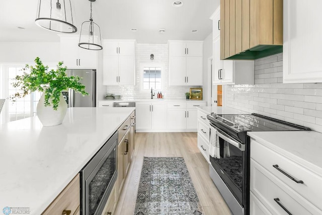 kitchen with appliances with stainless steel finishes, backsplash, light hardwood / wood-style floors, wall chimney exhaust hood, and pendant lighting