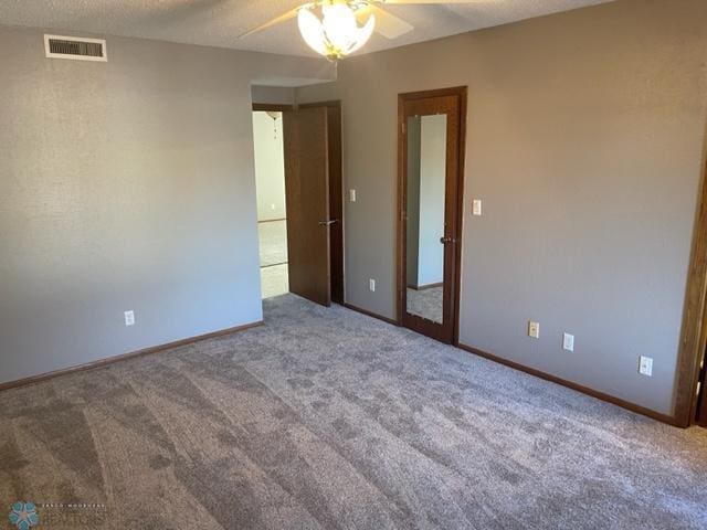 empty room featuring dark colored carpet, ceiling fan, and a textured ceiling