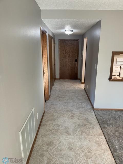 corridor with a textured ceiling and light tile flooring