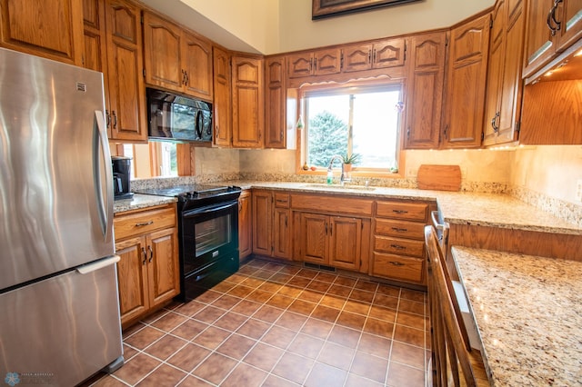 kitchen with dark tile flooring, black appliances, sink, and light stone countertops