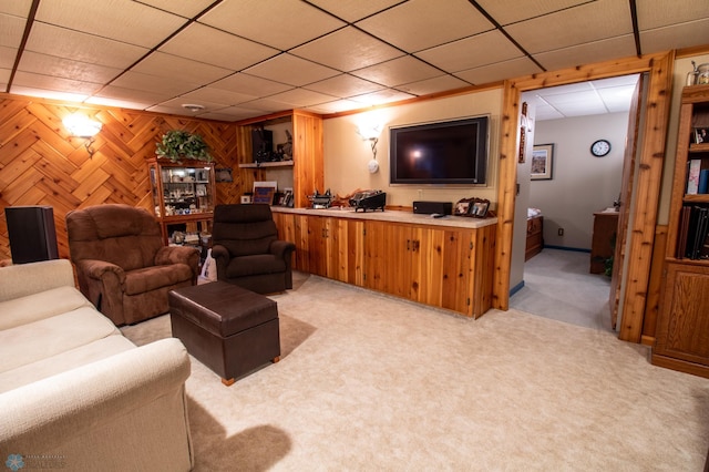 carpeted living room featuring a drop ceiling and wooden walls