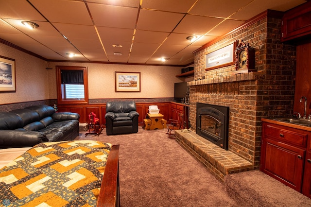 carpeted living room with sink, brick wall, a drop ceiling, and a fireplace