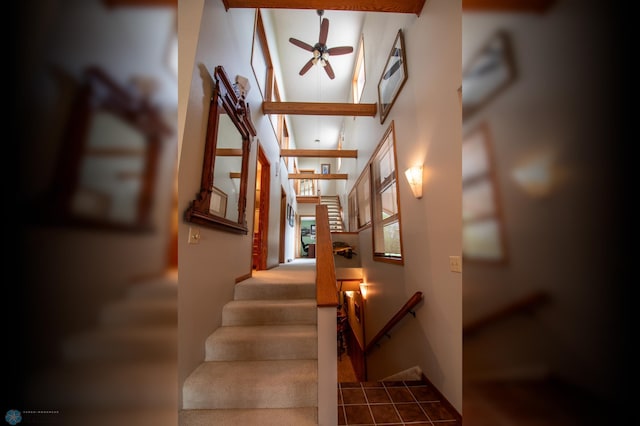 staircase featuring beamed ceiling, ceiling fan, and a towering ceiling