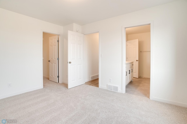 unfurnished bedroom featuring light carpet and connected bathroom